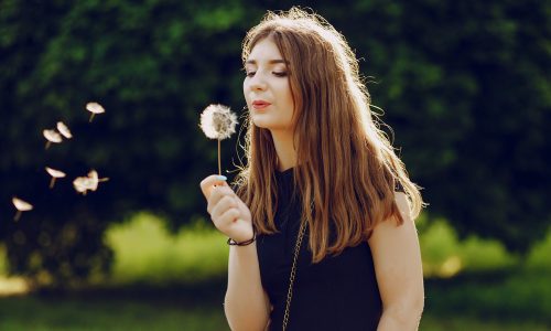 beautiful girl in a black dress walking in the summer sunshine park with dandelion