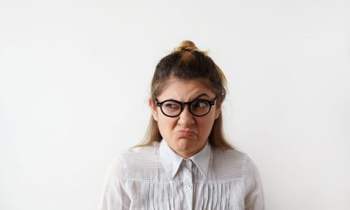 Female student looking offended, holding hands and frowning eyebrows. Her gloomy appearance says she is very unhappy and angry. Young female showing disapproval with pursed lips